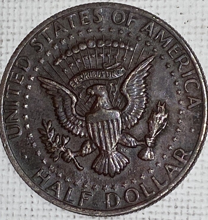 2004 Kennedy half dollar missing clad layer error showing copper-orange surface on one side where the outer nickel layer is absent